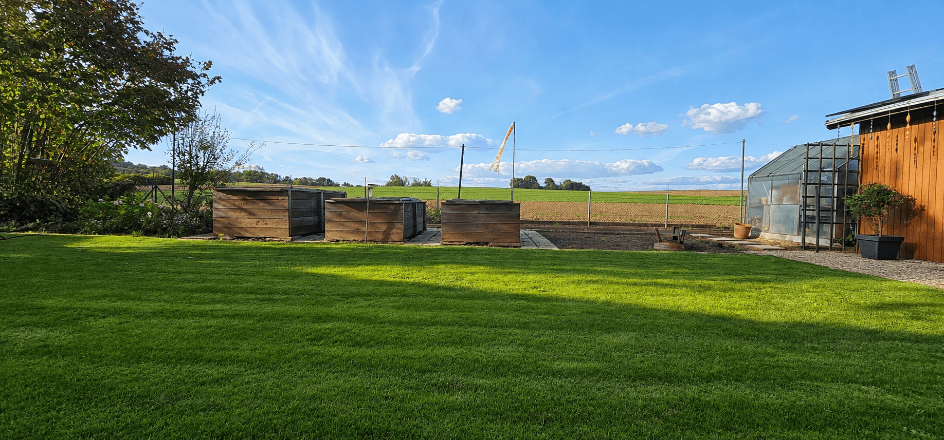 Gepflegter Garten mit Gewächshaus und Feldblick